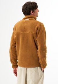 Braune Fleece-Pulloverjacke mit hohem Kragen, überschnittenen Schultern und strukturierter Stoff. Verfügt über ein hinteres Logetikett und einen geraden Saum.