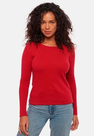 Pull rouge à manches longues avec un col rond, texture douce, coupe ajustée et poignets côtelés, associé à un jean en denim bleu clair.