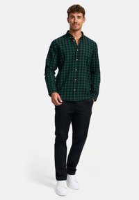Zelenočerná kostkovaná košile na knoflíky s límečkem, v kombinaci s tmavými kalhotami a bílými teniskami. Neformální design, přiléhavý silueta.