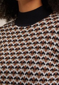 Stickad tröja med ett mönstrat design i bruna, svarta och vita färger. Hög hals med svart ribbad kant; mjuk textur.