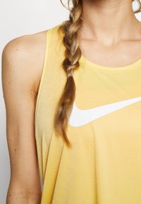 Żółta bezrękawnikowa koszulka sportowa o prążkowanej teksturze i dużym białym logo Nike na piersi, z okrągłym dekoltem.