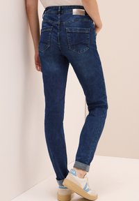 Donkerblauwe denim jeans met een slim fit, vijf zakken en omgeslagen enkels. Heeft een lichte wasbeurt en gestikte details op de achterzakken.