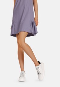 Abito viola con orlo arricciato, abbinato a sneaker bianche con occhielli in argento e un accento nero sul tallone. Tessuto dalla texture liscia.