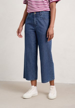 Wide-leg denim trousers in dark blue, featuring a high waist, two front pockets, and a button closure. Paired with white sneakers.