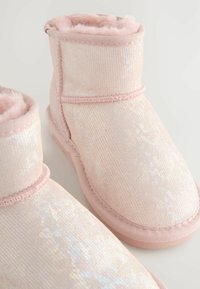 Un paio di pantofole invernali rosa, scintillanti e morbide, con foderatura in pile e punta arrotondata su uno sfondo chiaro.