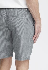 Grå og hvite stripete shorts laget av stoff med en teksturert overflate. Har to baklommer og et liv med dekorativt trim.