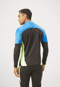 Langärmliges Sportshirt mit einer strukturierten blauen Oberseite, schwarzem Körper und limettengrünen Akzenten, hergestellt aus einem figurbetonten, atmungsaktiven Material.