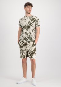 Pamučna tie-dye majica u bež i maslinasto zelenoj boji s kratkim rukavima, uparena s odgovarajućim šortsevima. Ima pojas s vezicom i prednje džepove.