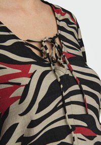 Top nero e rosso a motivo con scollatura a V e dettaglio con fiocco, realizzato in tessuto testurizzato con strisce beige e nere.