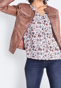 Brun läderjacka med rundad krage och två framfickor, över en blus med blommönster och mörkblå jeans.