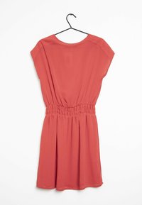 Robe corail à manches courtes, taille smockée élastique et jupe fluide. Texture lisse et tissu léger. Suspendue à un crochet noir.