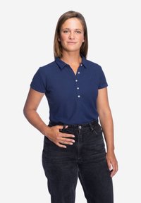 Marineblauw poloshirt met korte mouwen, een kraag en een sluiting met drie knopen, gecombineerd met hoge zwarte jeans. Subtiele logo op de borst.