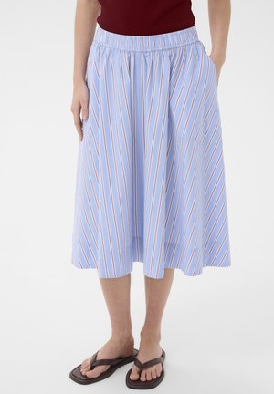 Jupe bleue mi-longue à rayures verticales rouges et blanches, taille élastique, portée avec des tongs marron foncé et un haut rouge.