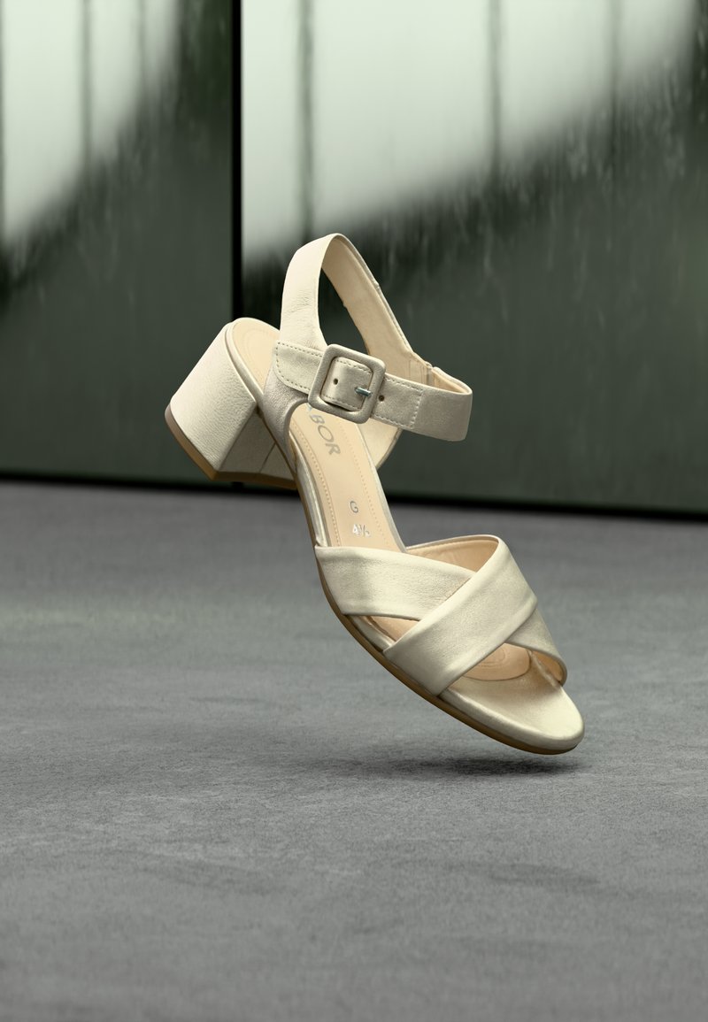 Sandale à talon beige avec une finition texturée, dotée de brides croisées, d'une bride à boucle autour de la cheville et d'un talon carré. Détail intérieur simple.