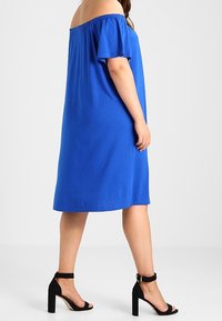 Sininen olkaimeton mekko, jossa on lyhyet hihat, rento leikkaus ja polvipituus. Yhdistetty mustiin korkeakorkoisiin sandaaleihin, joissa on nilkkahihnat.