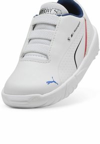 Baskets blanches avec une tige synthétique lisse, design à lacets, accents bleus, détails noirs et semelle texturée. Présente un logo sur le côté.