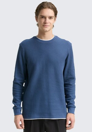 Blauwe geribbelde lange mouw shirt met een ronde hals en aansluitende manchetten. Gelaagd stof met een eenvoudig ontwerp en contrasterende binnenkraag.