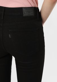 Jeans de mezclilla negros con una textura suave. Presentan una etiqueta de Levi Strauss & Co. y bolsillos traseros estándar con un diseño de costura curvada.