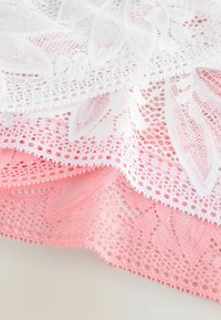 Spets tyg i vitt och rosa, med blommönster och intrikata öppna väverier. Mjuk textur, lagerdesign med vågiga kanter.