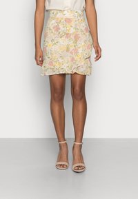 Blommig mönstrad minikjol med volangkant, i pastellrosa, gult och grönt på en ljus bakgrund. Lättviktsmaterial, figurnära design.