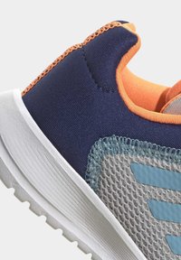 Chaussure de sport marine et grise avec un dessus en maille texturée. Présente des accents orange et une semelle en caoutchouc blanc avec un motif rainuré.