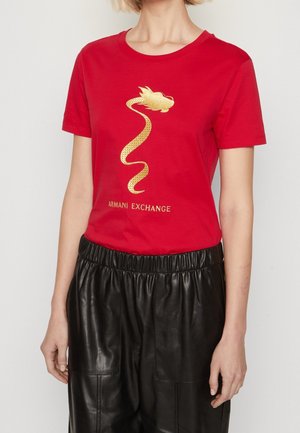 Persoon draagt een rood Armani Exchange T-shirt met een gouden draakontwerp en zwarte leren broek met hoge taille.