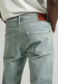 Jeans verdi menta sbiaditi caratterizzati da tasche posteriori con dettagli cuciti, una patch in pelle con logo e un design a gamba dritta.