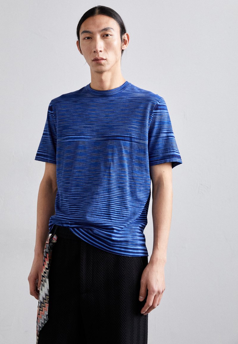 Blauwe gestreepte T-shirt met korte mouwen, gemaakt van textuurstof. Draagt bij zwarte geplaatste broek met een kleurrijke accenten.