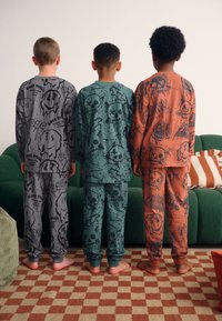 Pyjamas pour enfants en gris, bleu sarcelle et orange, avec des motifs graphiques de crânes et de visages souriants ; tissu en coton doux avec poignets élastiques.