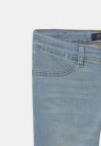 Light blue denim jeans with a smooth texture, featuring a classic design, five-pocket style, and stitched accents at the waist and seams.