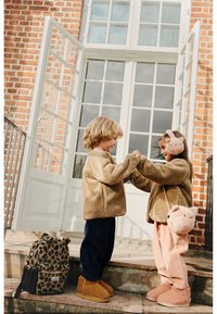 D dvojica djece u udobnim, bež flis jaknama stoje na stepenicama. Jedno nosi ružičaste kadifaste hlače i odgovarajuće krzneni čizme, držeći torbu u obliku mačke.
