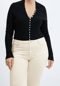 Cardigan nero a coste con scollatura a V profonda e maniche lunghe, caratterizzato da bottoni bianchi sul davanti. Abbinato a pantaloni beige aderenti.
