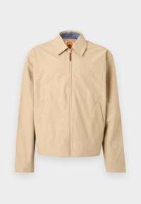 Μπεζ μπουφάν με φερμουάρ και γιακά, πλαϊνές τσέπες και κεντημένο λογότυπο στο στήθος, με μπλε καρό εσωτερική επένδυση.