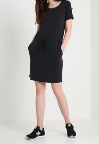 Robe noire à manches courtes avec taille cordon, poches et coupe décontractée, associée à des baskets noires avec des accents blancs.