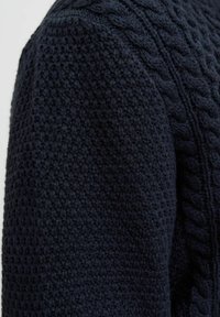 Donkerblauwe gebreide trui met een textuurpatroon en kabelbrei-details. Gemaakt van zacht, warm materiaal. Close-up zicht.