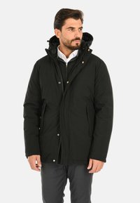 Giacca nera isolante con cappuccio staccabile, chiusura frontale con zip, tasche laterali e dettagli con bottoni a pressione. Materiale esterno liscio, fitting casual.