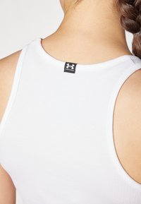 Biały sportowy top na ramiączkach z prążkowanej tkaniny, z czarną metką logo Under Armour z tyłu kołnierza.