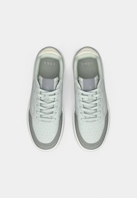 Svetlo šedé tenisky s perforovaným koženým dizajnom, s šedými akcentmi a rovnými šnúrkami, umiestnené na bielom pozadí.