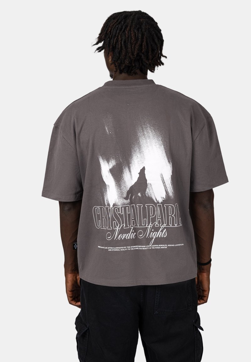 Šedé oversize tričko s bílou grafikou, na kterou je silueta vlka a text "CRYSTALPARK Nordic Nights" na zadní straně, krátké rukávy.