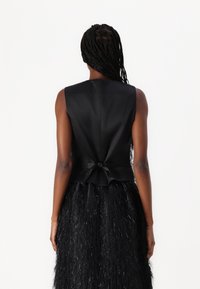 Black satin sleeveless top with a bow at the back, paired with a black textured skirt featuring a feathery appearance and shine.