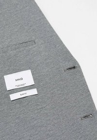 Tessuto grigio slim-fit con una sottile texture, dotato di due etichette: una per il marchio "MNG" e l'altra contrassegnata "SLIM FIT."
