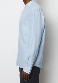 Vaaleansininen pitkähihaonen paita, joka on valmistettu pellavasta. Siinä on bändikaulus sekä rintatasku, ja hihoissa ja sivussa on napit.