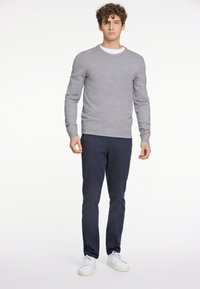 Grå stickad tröja med rund halsringning, bärs över en vit skjorta, kombinerad med marinblå chinos och vita sneakers.