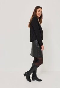 Fekete blézer, testhez simuló bőrszoknya és térd fölé érő fekete csizma, textúrázott díszítéssel. Egyszerű dizájn, sima bőr és egyszínű színek.