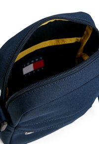 Borsa in tessuto blu marino con apertura con cerniera, interno giallo e etichetta con il logo Tommy Hilfiger in rosso, bianco e blu. Materiale con texture.