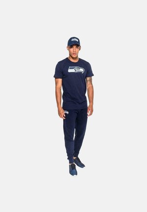 Navy blue Seattle Seahawks athletic outfit, featuring a short-sleeve t-shirt with logo and matching joggers with logo detail, worn with a cap.