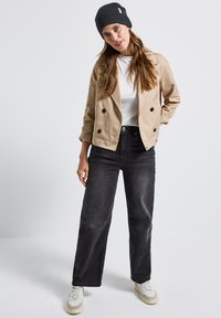 Béžový dvouřadý kabát, bílý tričko, černé široké džíny, šedý pletený čepice a krémové tenisky s jemnými akcenty. Jednoduchý, neformální outfit.