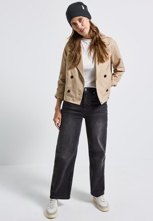 Giacca beige doppiopetto, t-shirt bianca, jeans neri a gamba larga, berretto grigio a maglia e sneakers crema con leggeri accenti chiari. Outfit semplice e casual.
