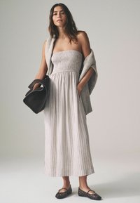 Lichtgrijze strapless jurk met een gesmockte buste en verticale strepen; gecombineerd met een grijze sjaal en een zwarte handtas. Zwarte geweven ballerina's maken de look compleet.