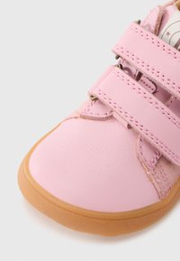 Ροζ δερμάτινο παπούτσι με δύο λουράκια βέλκρο, στρογγυλεμένη μύτη και υφασμένη σόλα από καουτσούκ. Ορατές λεπτομέρειες ραφής κοντά στα λουράκια.